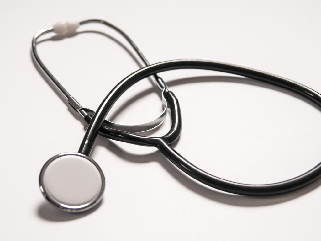 A black and silver stethoscope with a round diaphragm lies on a plain, white surface. The stethoscope is coiled, with its earpieces and tubing visible, creating a simple and clean composition.