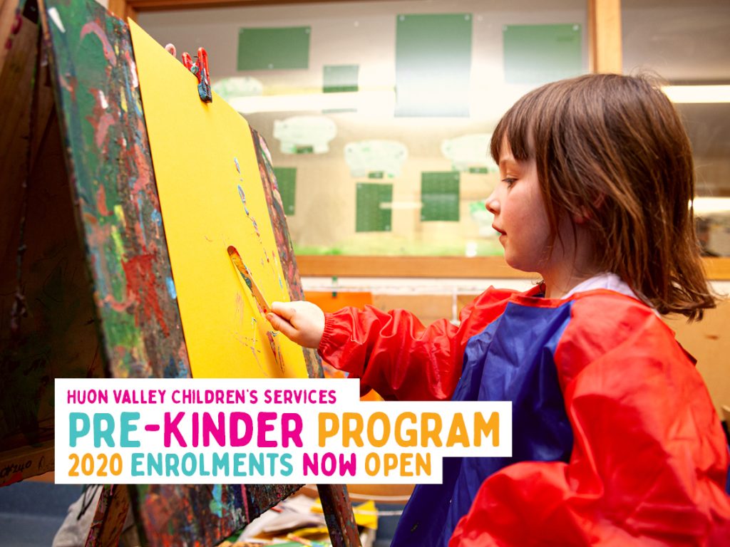 A child in a red and blue apron paints on a yellow canvas at an easel. Text on the image reads, Huon Valley Childrens Services Pre-Kinder Program 2020 Enrolments Now Open. The background shows shelves and art supplies.