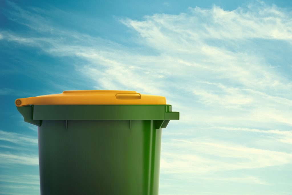 A green trash bin with a yellow lid is placed against a backdrop of a blue sky with scattered clouds.