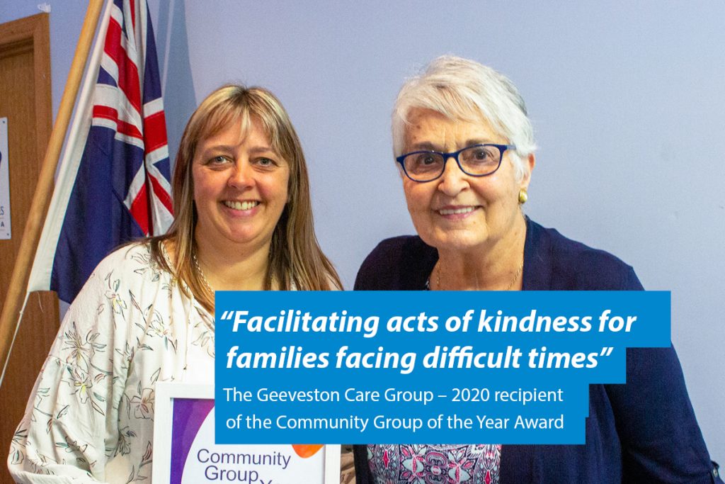 Two women smile together; one holds a plaque. A banner reads, “Facilitating acts of kindness for families facing difficult times,” noting the Geeveston Care Group as the 2020 Community Group of the Year Award recipient. An Australian flag is visible.