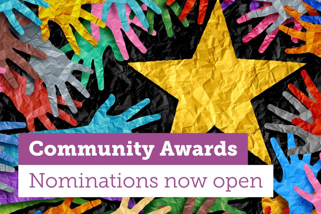 Colorful paper hands and a large yellow star on a crumpled black background. Text reads Community Awards in white on a purple banner, and Nominations now open in purple below.