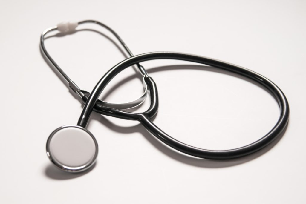 A black stethoscope with a silver diaphragm and earpieces is coiled on a white surface. Its tubing loops, and the chest piece is prominently visible in the foreground.