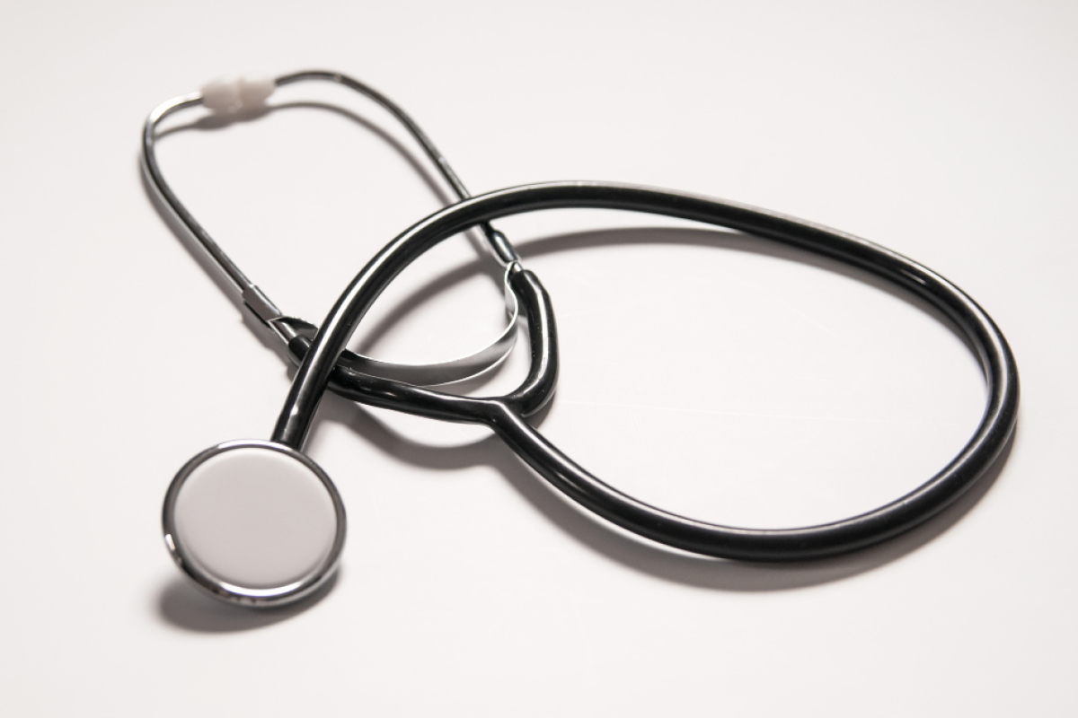A stethoscope with black tubing and silver accents is coiled on a white surface. The diaphragm and earpieces are visible, highlighting its use as a medical instrument.