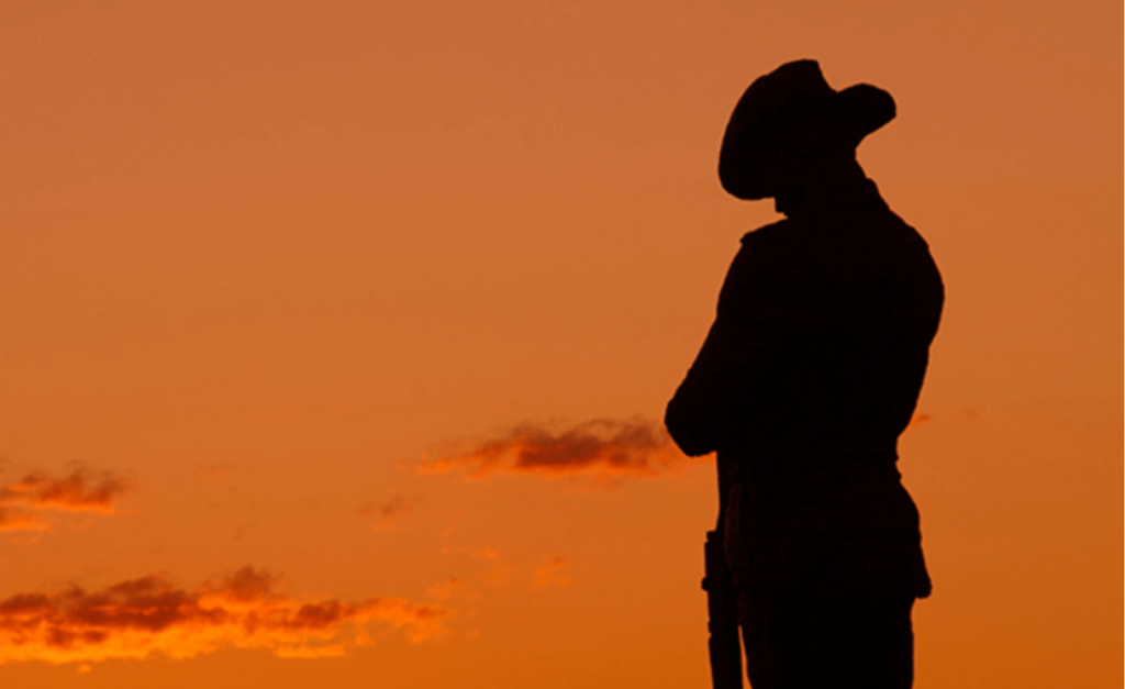 Silhouette of a soldier in uniform and hat, standing against a dramatic orange sunset sky. The soldier is holding a rifle, creating a solemn and reflective scene.
