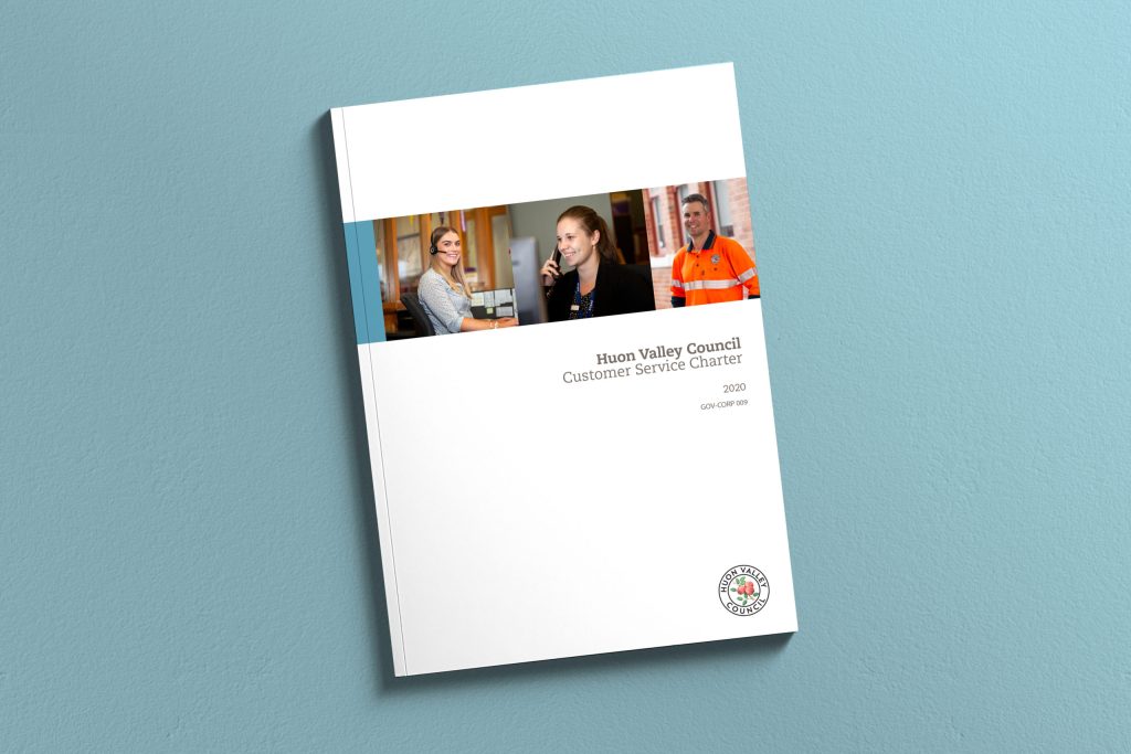 Cover of a booklet titled Huon Valley Council Customer Service Charter 2020. It features three small photos of smiling individuals engaged in various activities and displays a council logo in the bottom right corner, all on a blue background.