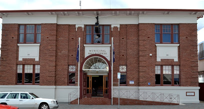 A two-story brick building with large windows and a central entrance marked Municipal Hall & Offices. Three flagpoles stand outside, and a white car is parked in front.