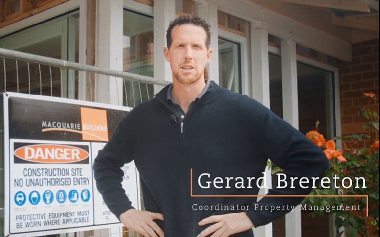 A person stands in front of a construction site sign, which includes safety warnings. They are wearing a dark sweater and have their hands on their hips. Text on the image reads, “Gerard Brereton, Coordinator Property Management.”.