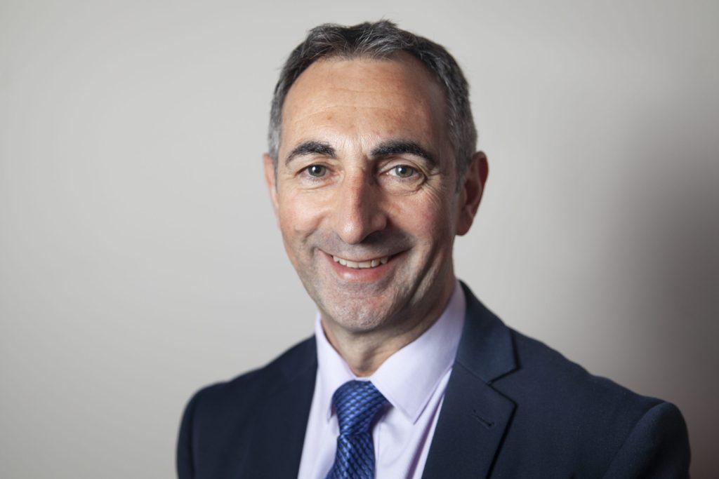 Man in a suit and tie smiling at the camera against a plain background.