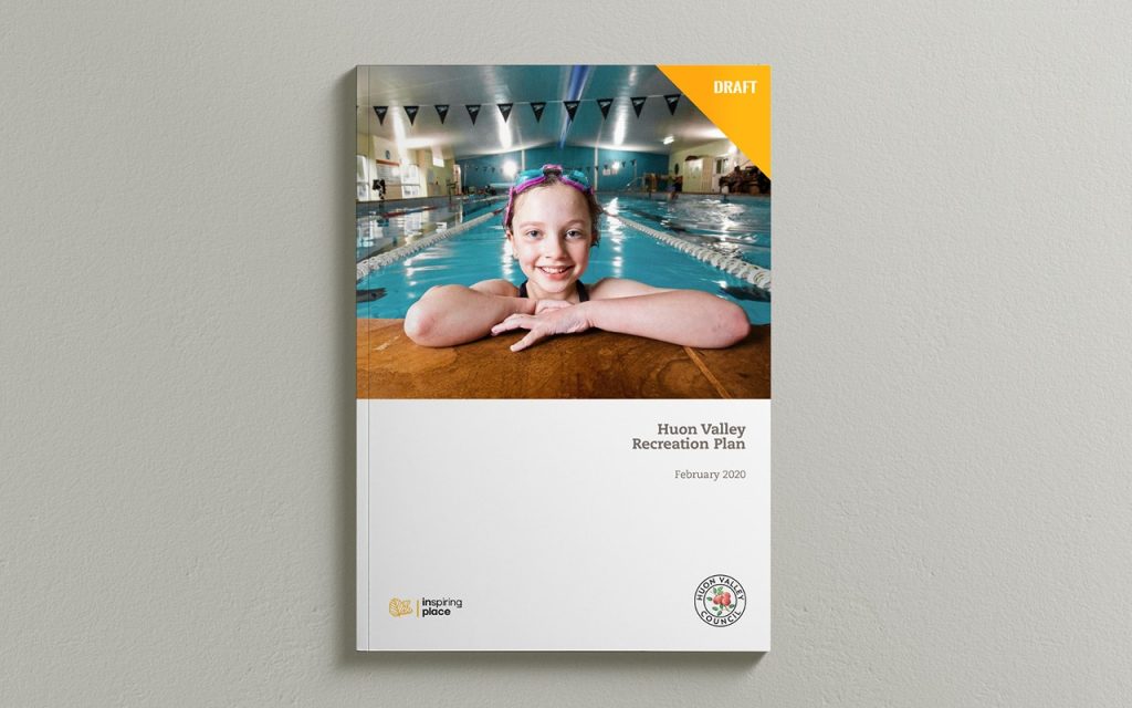 A book titled Huon Valley Recreation Plan with a cover image of a smiling child resting on the edge of an indoor swimming pool. The top right corner has an orange label that reads DRAFT. The date February 2020 is below the title.