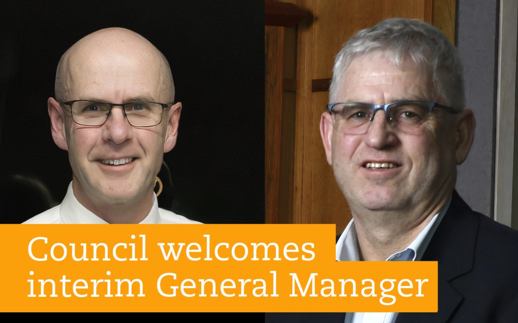 Two men are pictured side by side. Both are wearing glasses and formal attire. The text overlaid says, Council welcomes interim General Manager. The background on the left is dark, while the right side has a wooden surface.