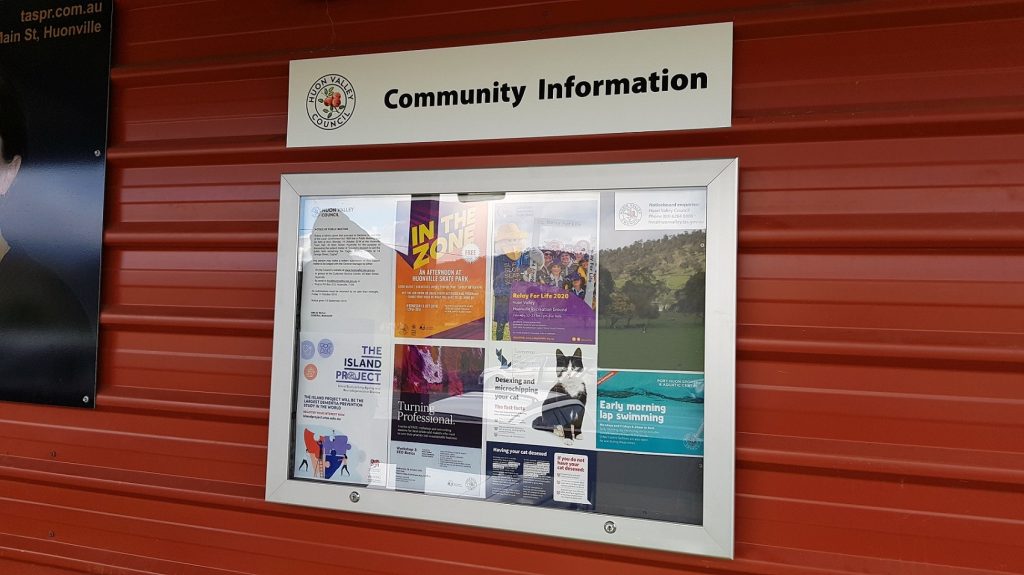Bulletin board titled Community Information on a red wall, displaying various posters and flyers about local events, projects, and activities, including ones about a music festival and a community project.