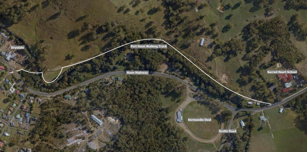 Aerial view of a landscape showing the Port Huon Walking Track outlined in white. Surrounding features include trees, the Huon Highway, buildings, Drysdale, Sacred Heart School, Kermandie Oval, and Scotts Road.