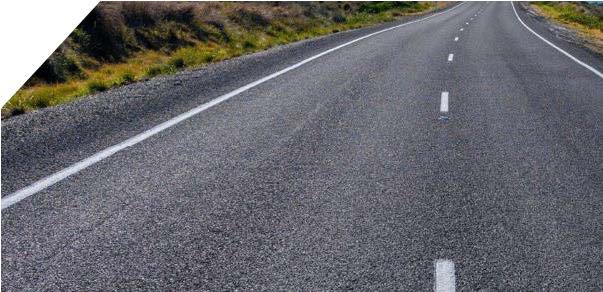 An empty, paved road stretches into the distance, bordered by grass and shrubs. The road has clear white lines and appears to be in a rural setting. The sky is not visible.