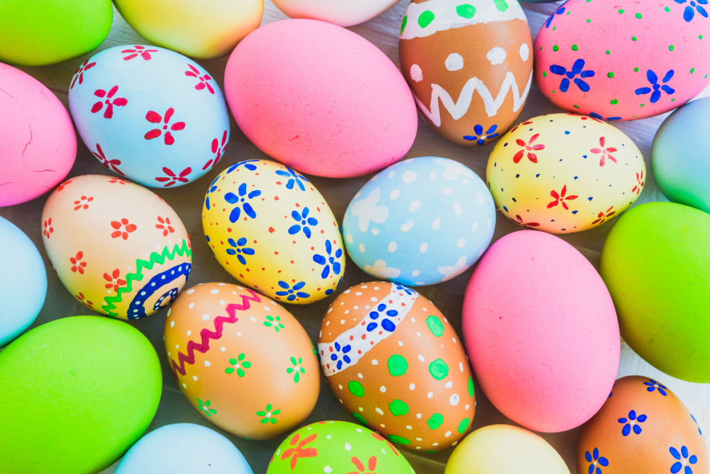 A collection of colorful Easter eggs, each uniquely decorated with patterns like flowers, dots, and zigzags. The eggs are in vibrant colors such as pink, blue, green, and yellow, creating a festive and cheerful display.