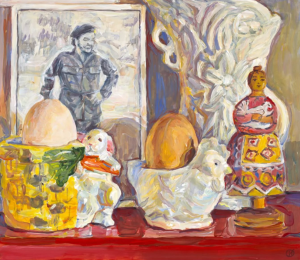 A colorful still life painting features two eggs in decorative holders, a figurine of a woman in a patterned dress, a lamb ornament, and a black-and-white photo of a man in uniform, all set against a bright, textured backdrop.