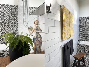 A bathroom with black and white patterned tiles, a white subway tile wall, a potted fern, a decorative figurine, yellow patterned towels, a black towel, and a wooden stool near a bathtub.