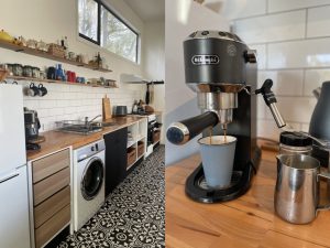 A modern kitchen with patterned floor tiles, wooden countertops, open shelves with dishes, and a close-up of a De’Longhi espresso machine making coffee into a blue cup.
