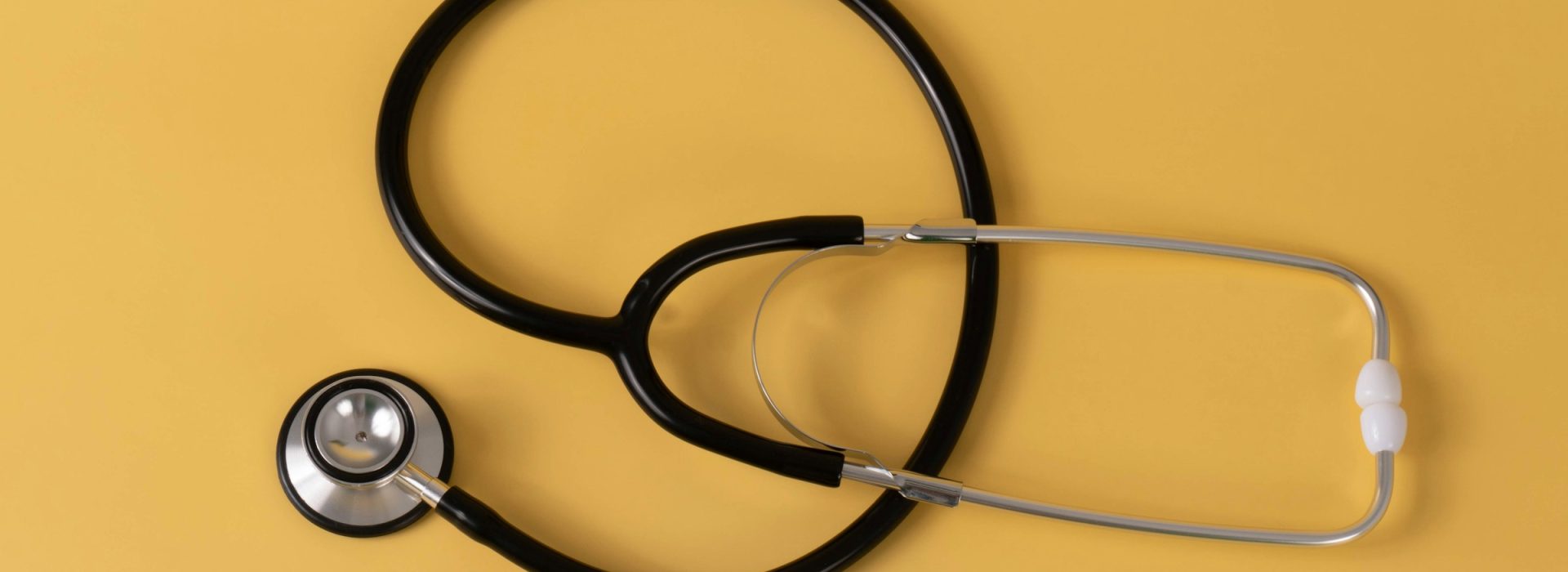 A black and silver stethoscope is arranged in a loose spiral on a solid yellow background.