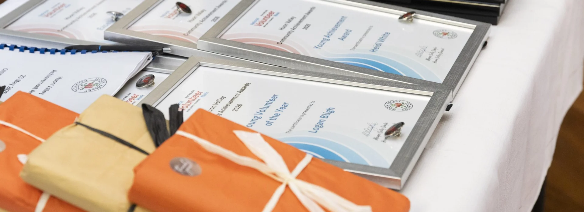 A table displays framed volunteer award certificates and several wrapped gifts in orange and brown paper, all prepared for a recognition event.