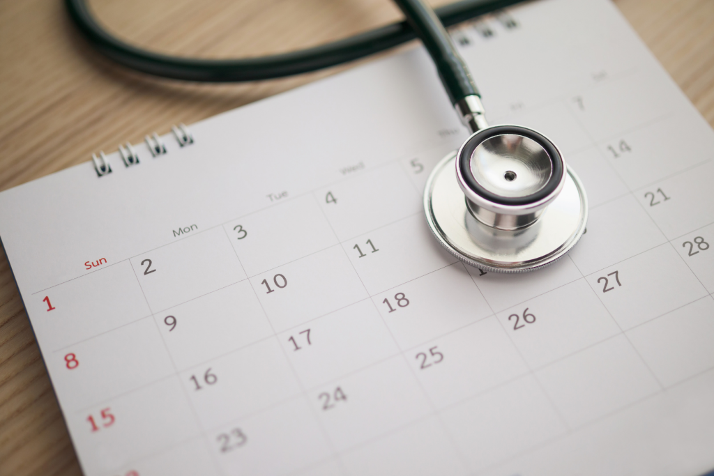 A stethoscope rests on top of an open calendar, symbolizing the scheduling of a medical appointment or healthcare planning.
