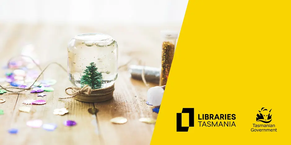A handmade snow globe with a small tree inside sits on a wooden surface scattered with colorful confetti. Beside it are vials of glitter. The right side has a yellow background with Libraries Tasmania and Tasmanian Government logos.