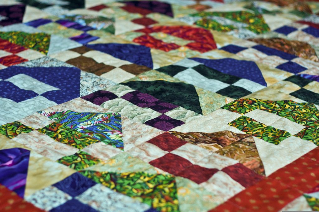 A colorful patchwork quilt featuring various geometric patterns and vibrant fabric squares in red, green, purple, blue, and cream tones.
