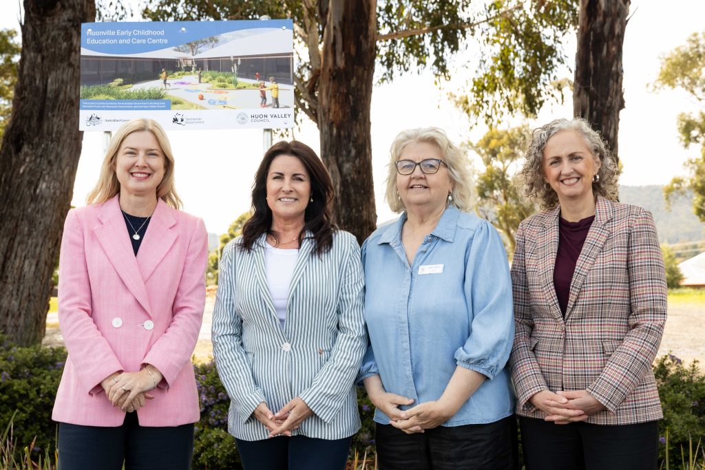 Four women standing together outdoors in front of a sign for the Huonville Early Childhood Education and Care Centre.