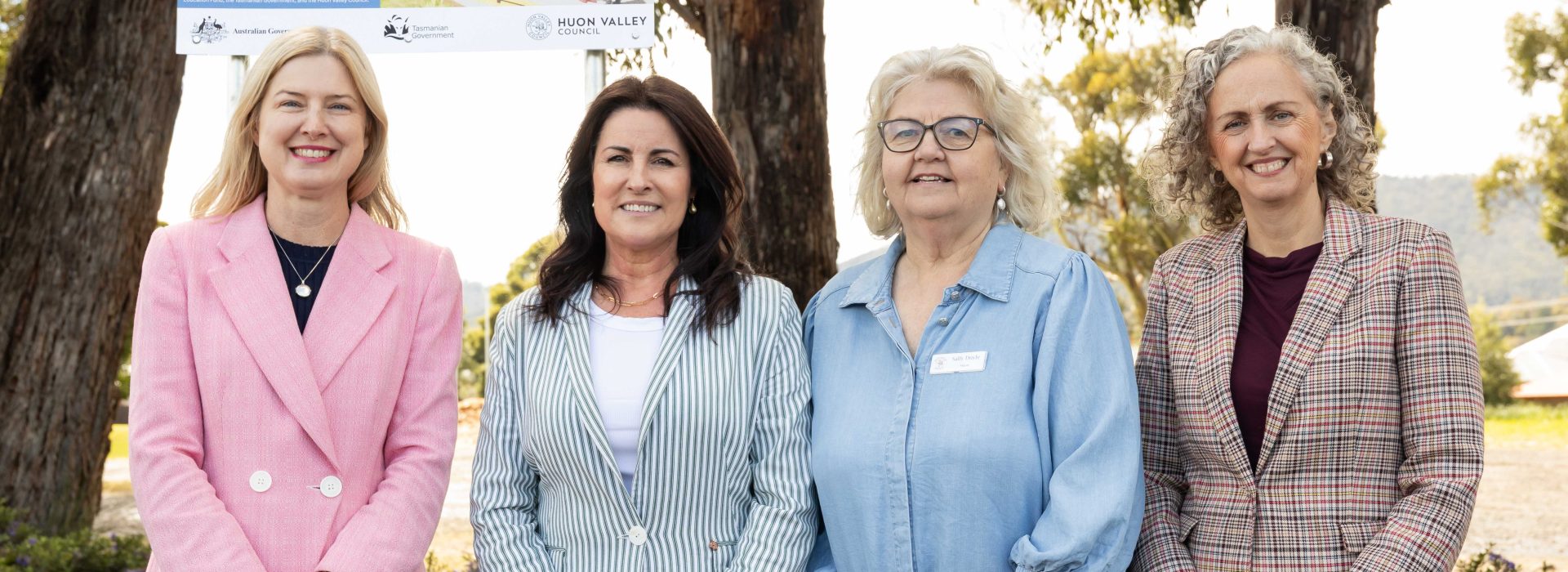 Four women standing together outdoors in front of a sign for the Huonville Early Childhood Education and Care Centre.